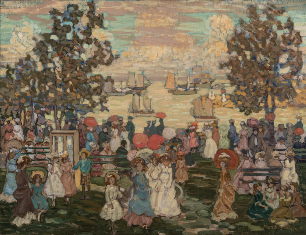 A large crowd of people in a city park near a large body of water. There are several boats in the water.