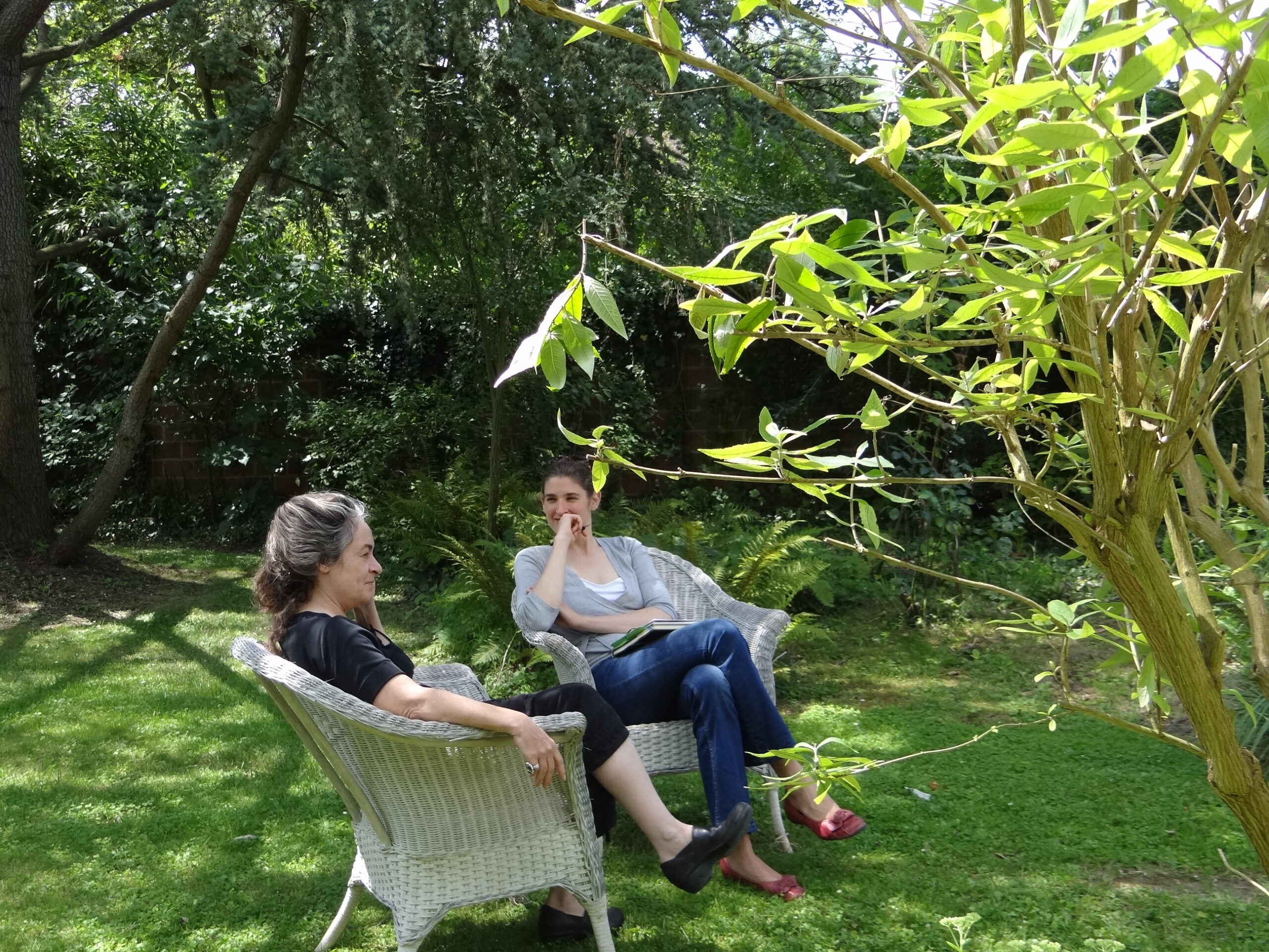 Two people seated in chairs in a garden.