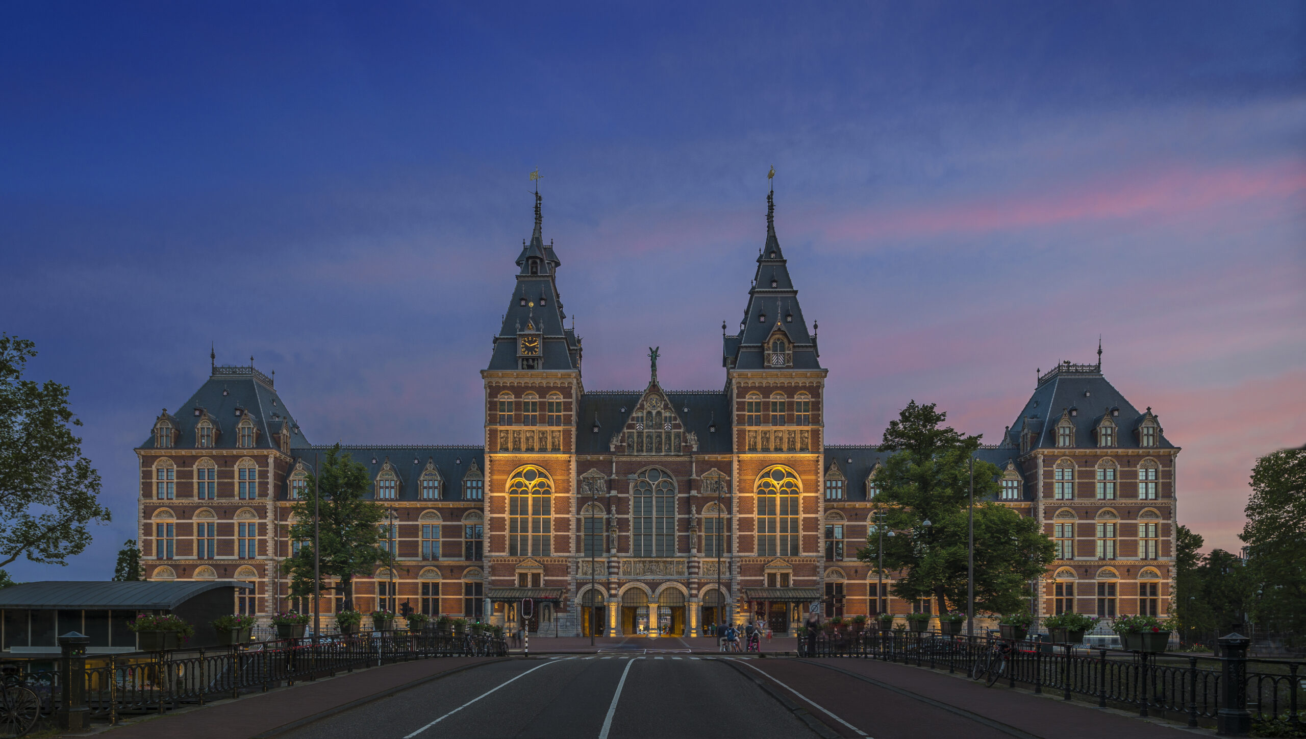 An ornate building pictured in the evening. It is lit from below and the sky is shades of blue and pink.