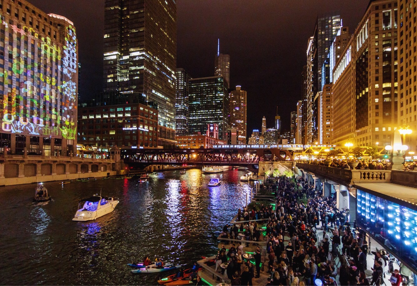 Image of the city and Chicago River at night. The buildings are lit up and reflected in the river.