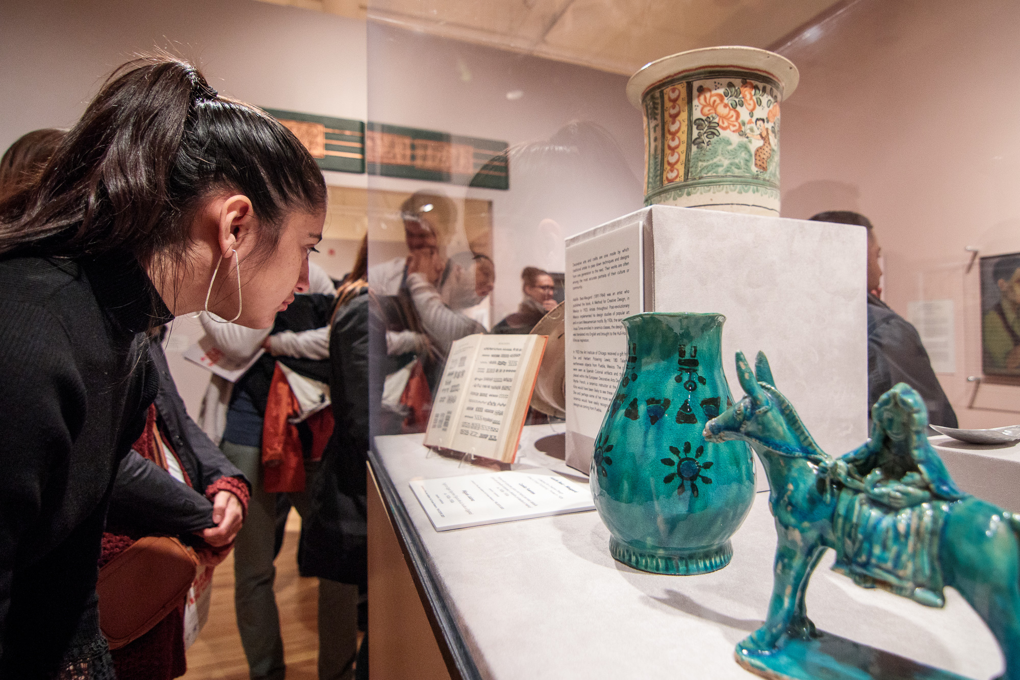 A person looks into a plexiglass case housing teal-colored ceramics.