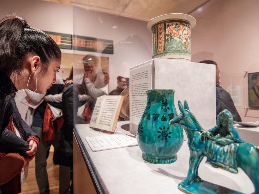 A person looks into a plexiglass case housing teal-colored ceramics.