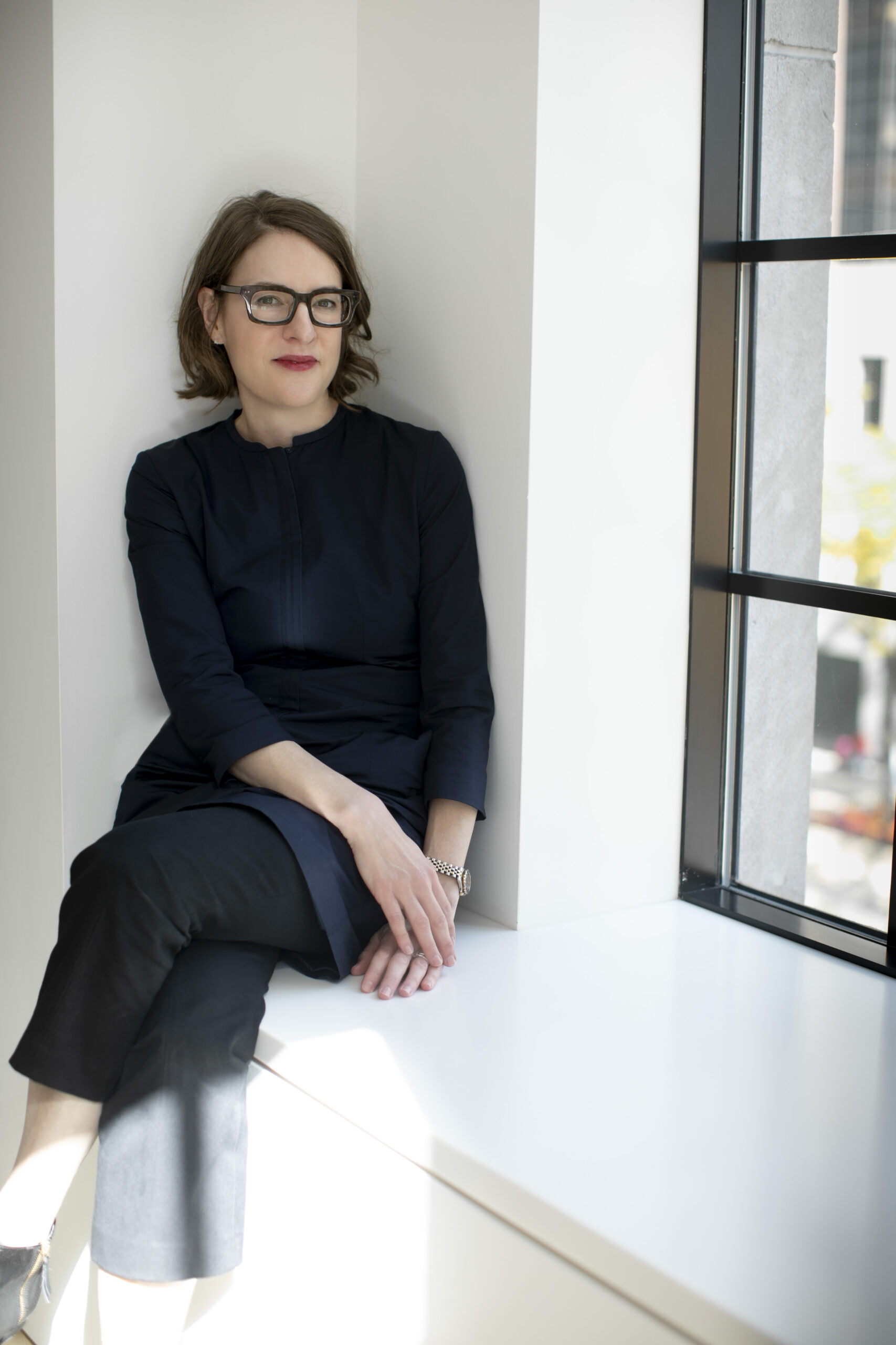 Photo of Sharon Corwin, Terra Foundation President and CEO. She is seated on a window sill with her legs crossed. She has short brown hair, is wearing glasses, and has a subtle smile.