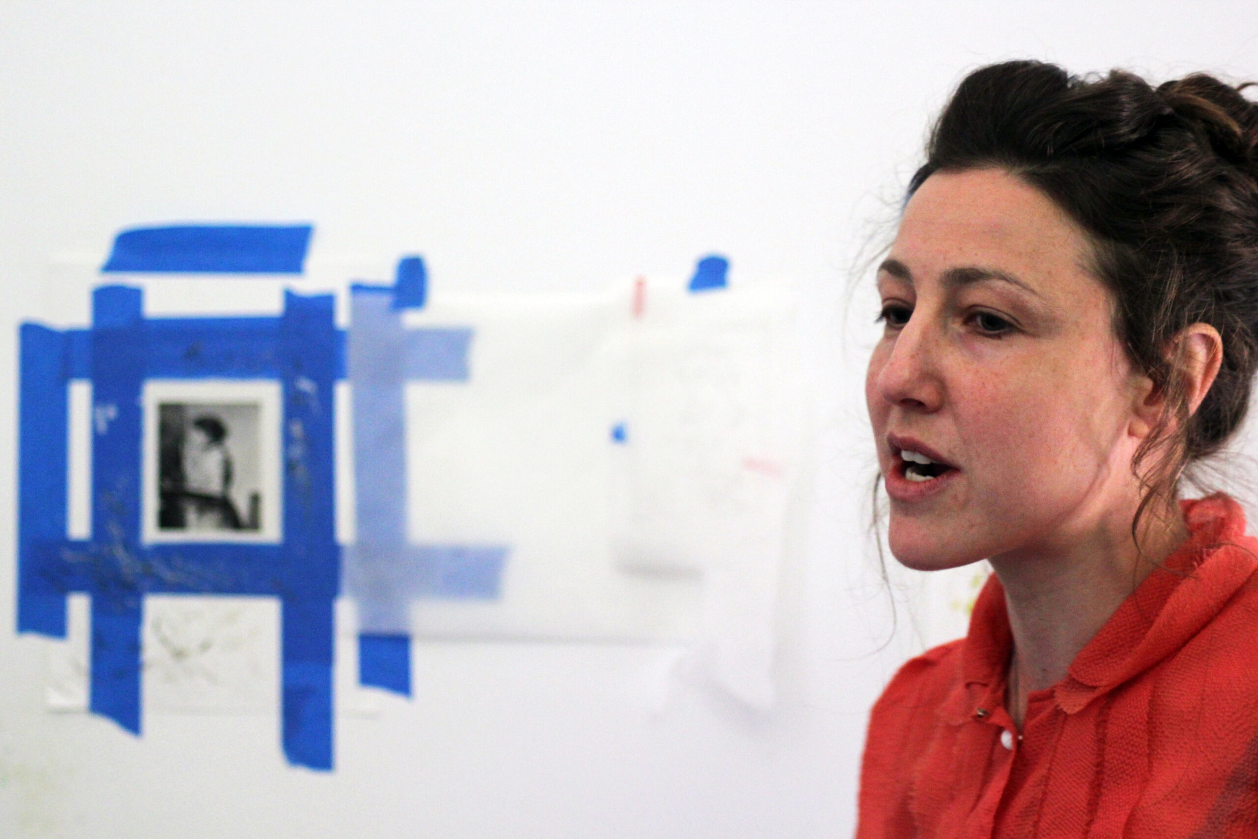 Woman talking with an artwork behind her.