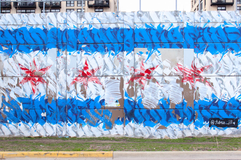 Photo of graffiti on a wall created with types forms. The graffiti resembles the Chicago flag. There are white and blue horizontal stripes with four red stars in the center.