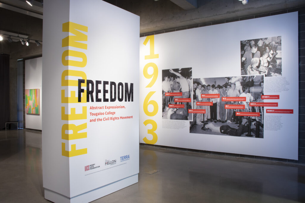 White gallery walls with black and white photographs installed. The exhibition title is set in large type on the nearest wall an says "Installation view FREEDOM: Abstract Expressionism, Tougaloo College and the Civil Rights Movement."