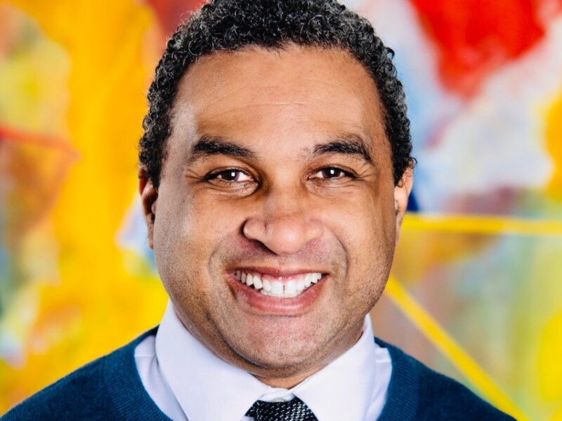 Headshot against a multicolored background.