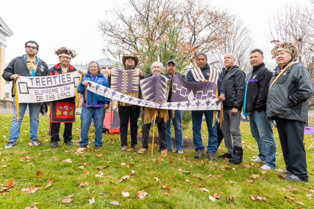 Photograph of a group of people standing in a row holding purple and white wampum.