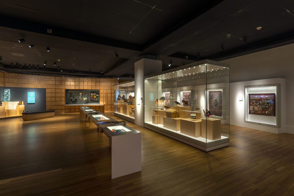 A gallery installation featuring Native American objects in brightly lit glass cases.