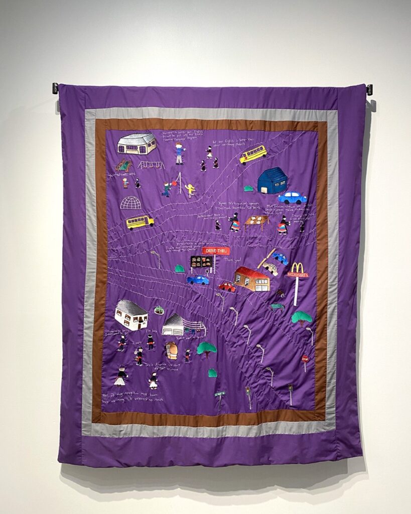 A purple quilt with embroidered imagery titled Becoming White, by artist Ger Xiong.