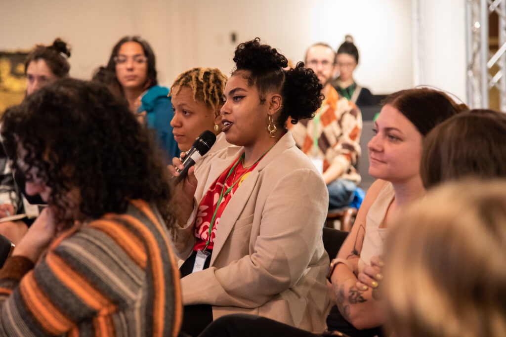 Person seated in a crowd asking a question into a microphone.