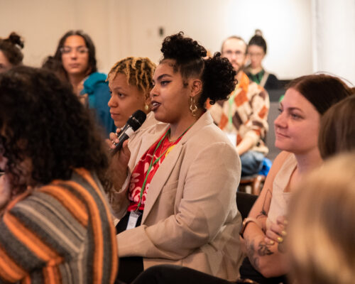 Person seated in a crowd asking a question into a microphone.