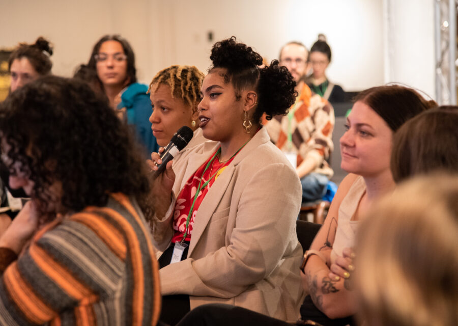 Person seated in a crowd asking a question into a microphone.
