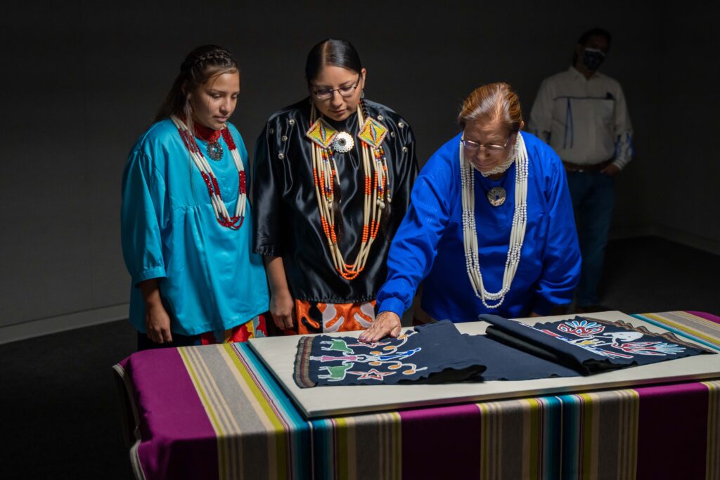 A picture of three people looking at a breechcloth on a table.
