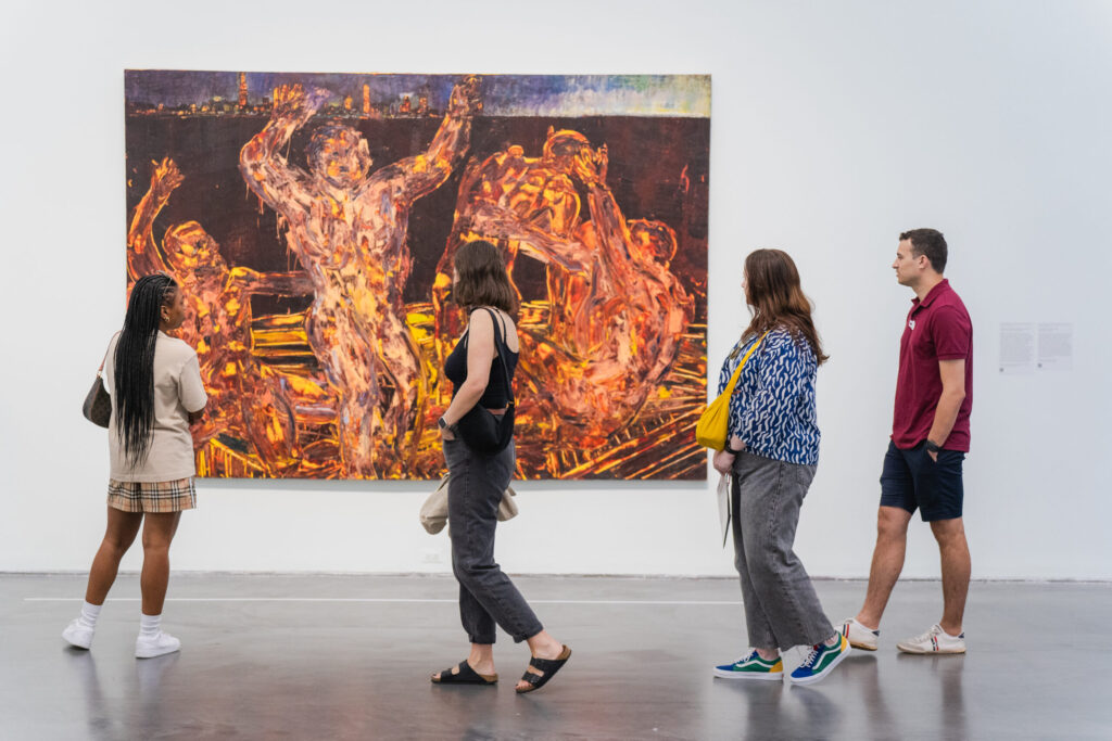 A group of people looking at a painting on a wall as they walk by at an exhibition.