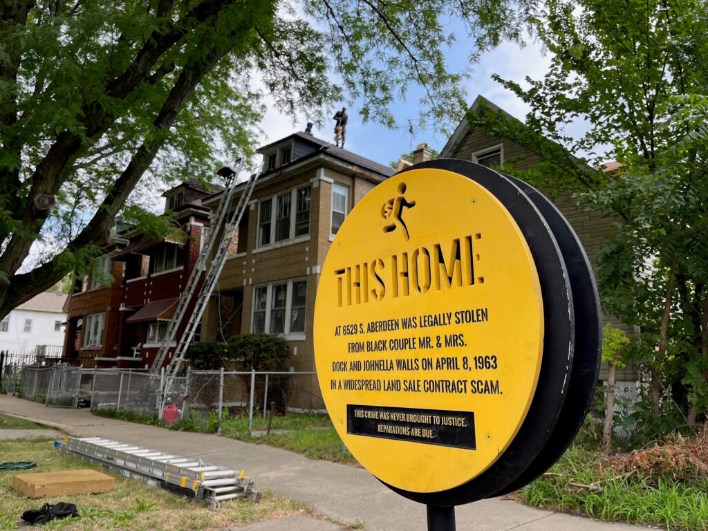 Yellow sign in front of a row of homes that says, "This Home: at 6529 S. Aberdeen was legally stolen from Black couple Mr. & Mrs. Dock and Johnella Walls on April 8, 1963 in a widespread land sale contract scam."
