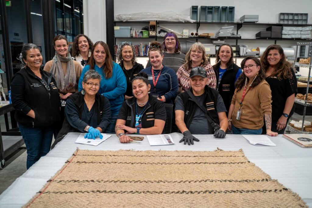 A group of people sitting together smiling in front of a wool textile set on a table.