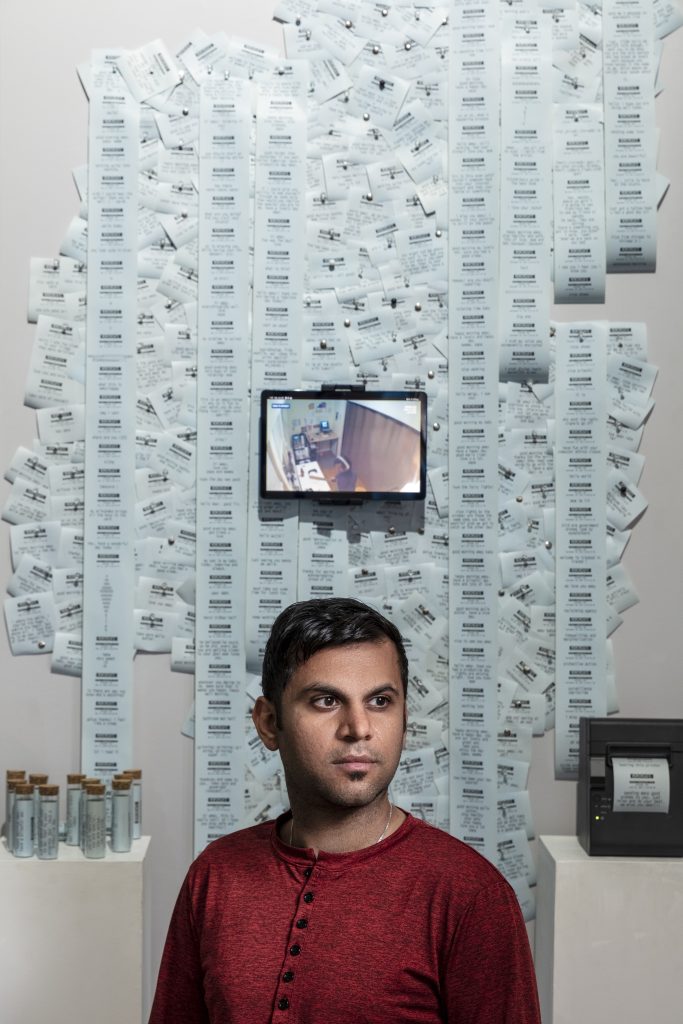 Image of person with a red sweater standing in front of a wall of paper.