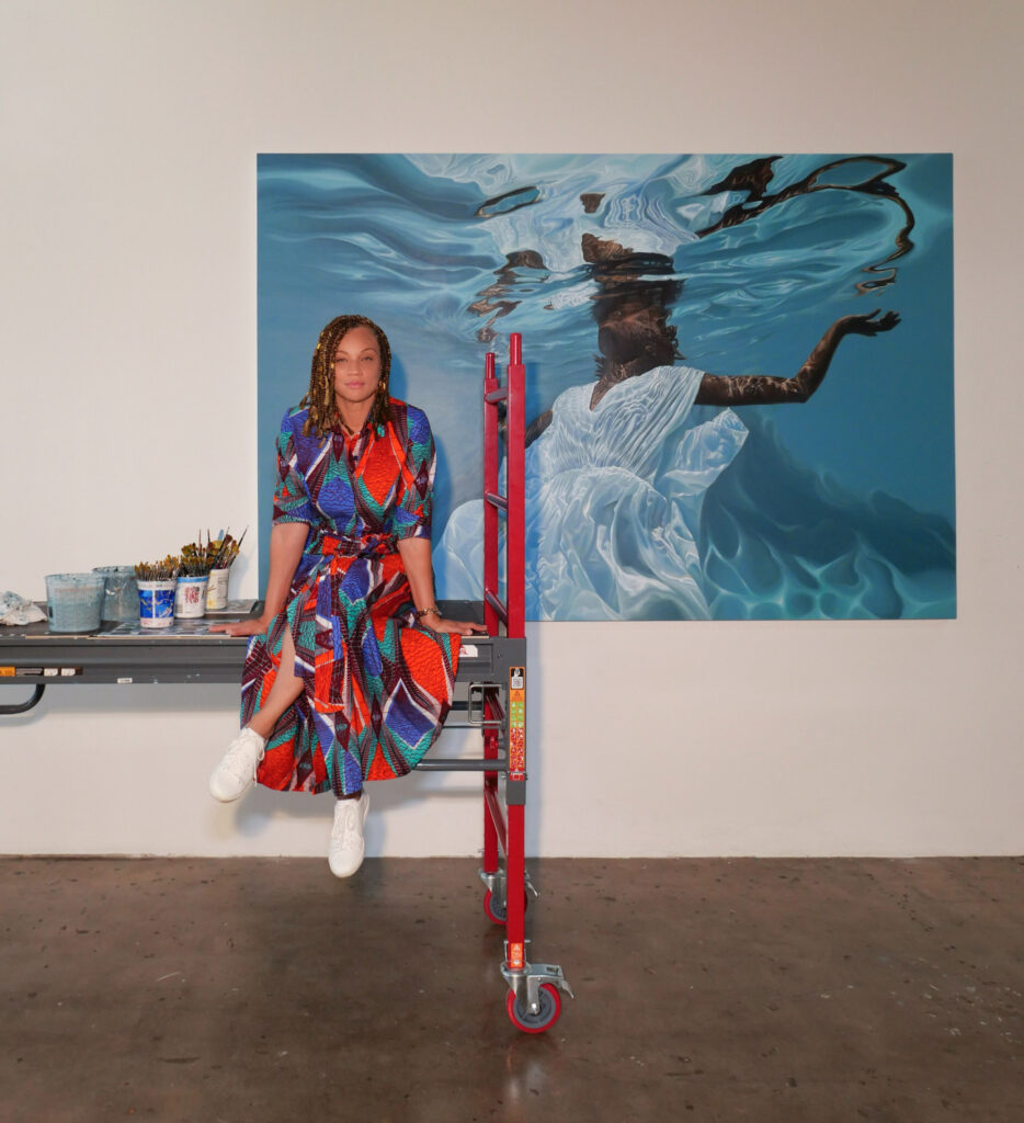 Image of person in a colorful dress sitting in front of blue artwork at an exhibition.