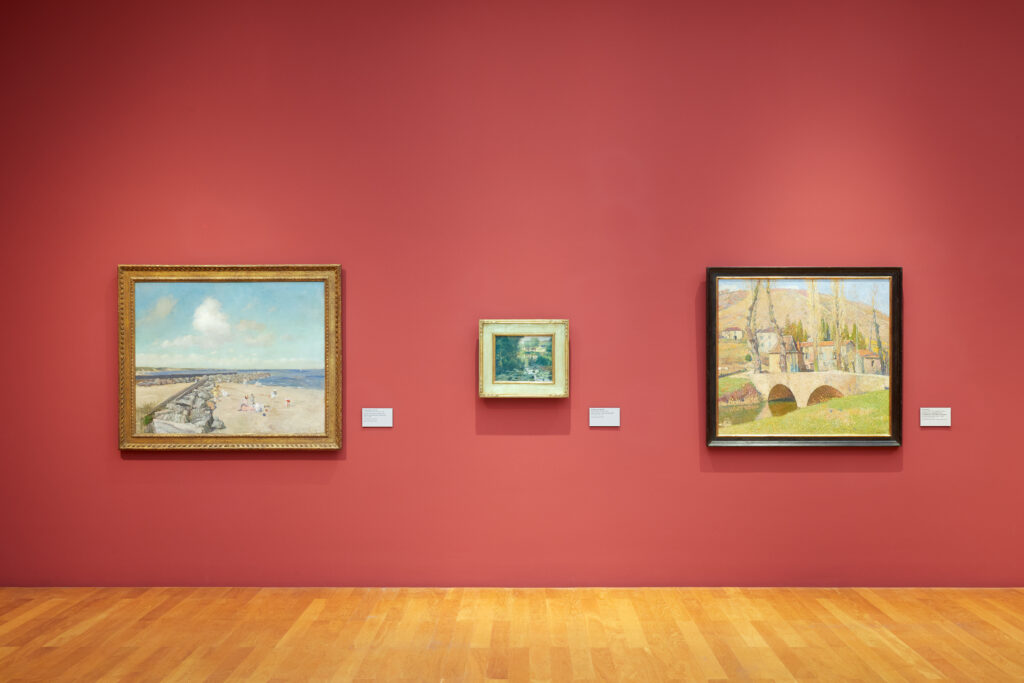 An art gallery red wall with three different art pieces in a row, featuring two larger objects and a smaller object in between them.