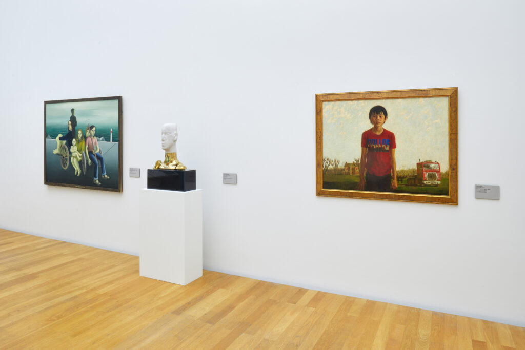 An art gallery wall with three different art pieces on it, featuring two framed objects on each side and a head-shaped figure on a stand in the center.