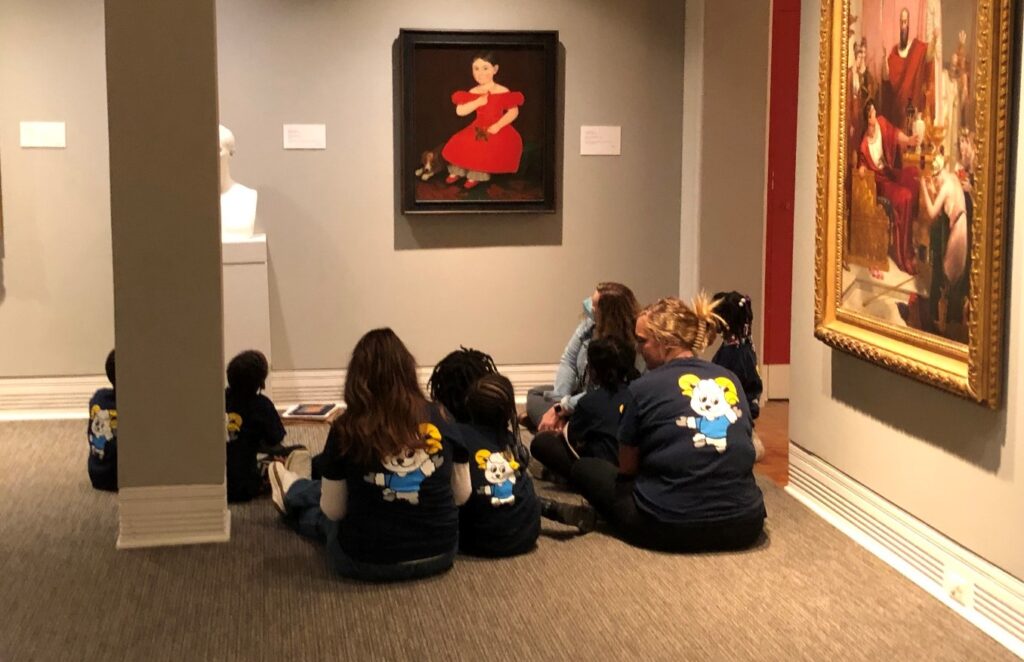 Group of children sitting around an artpiece at a museum.