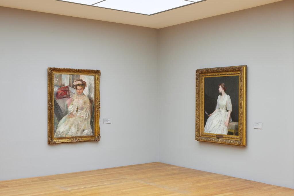 The corner of an art gallery room with framed art objects on each side of the wall.