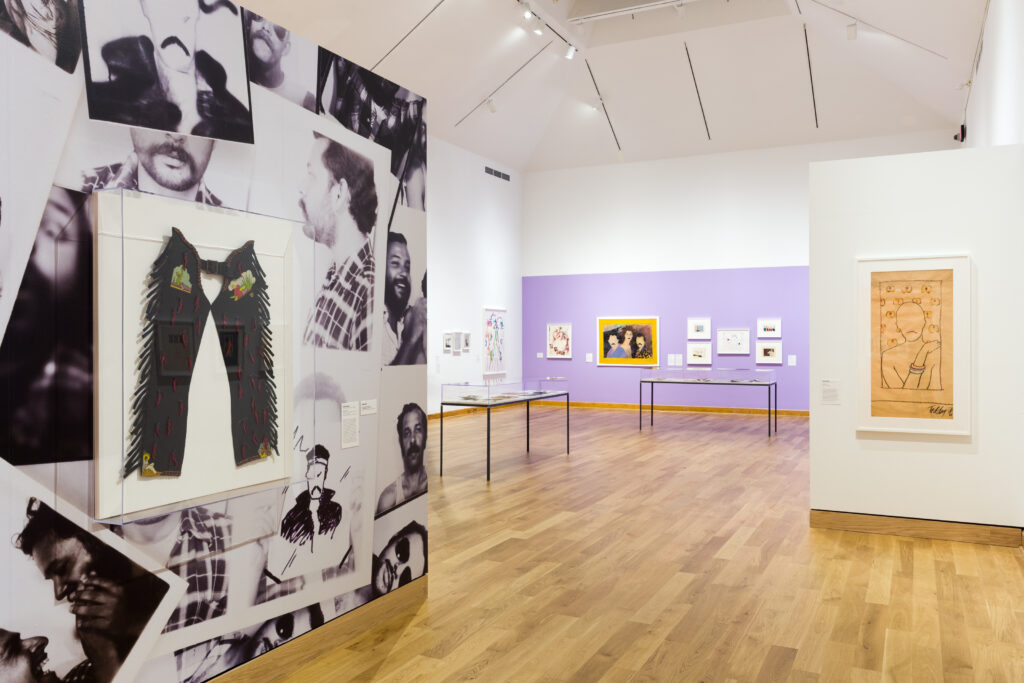 Objects hanging on gallery walls, with one wall wallpapered and one painted light purple.