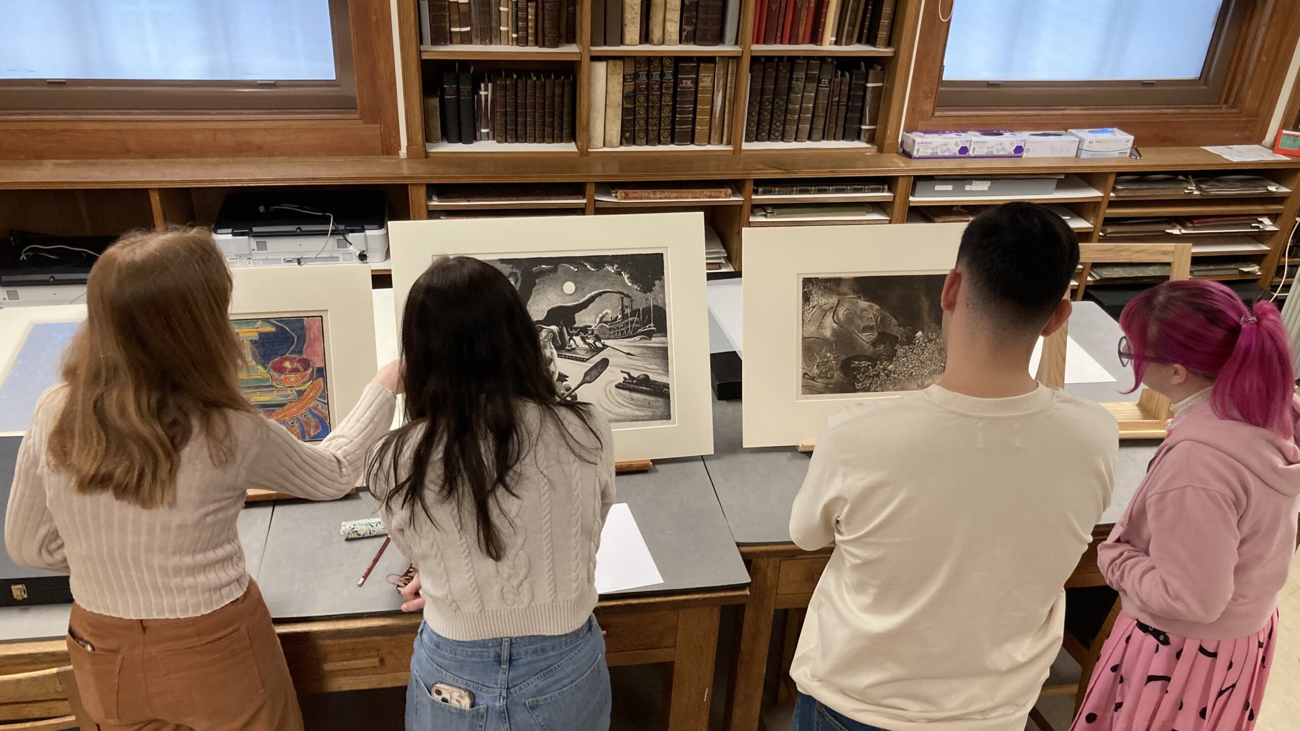 A group of people viewing a table with multiple art pieces on it.