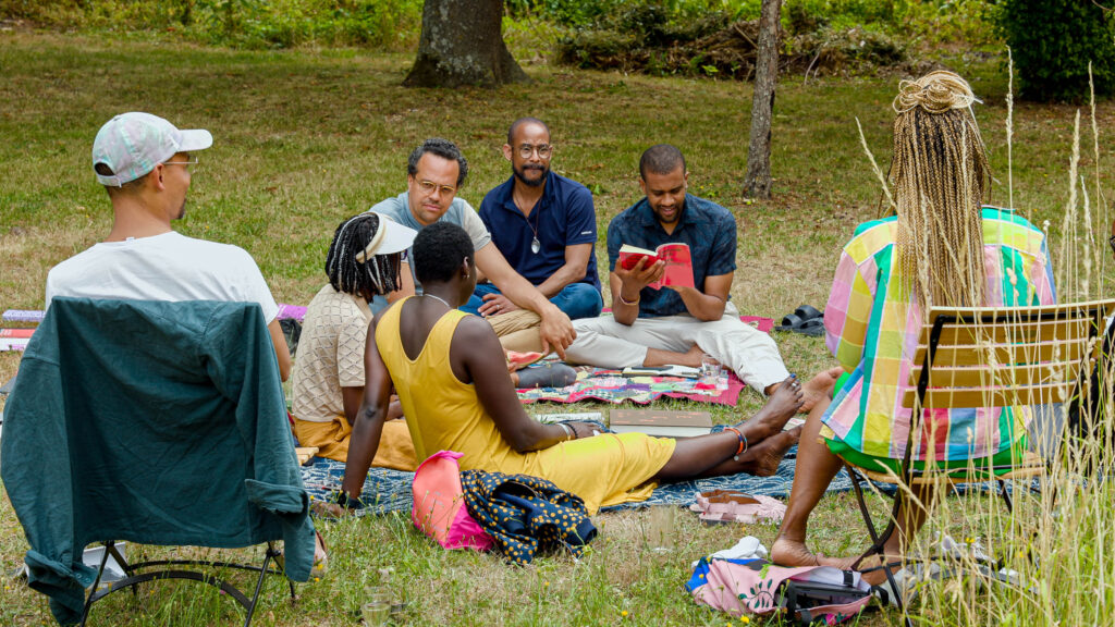 Group of people seated on a blanket on the grass.