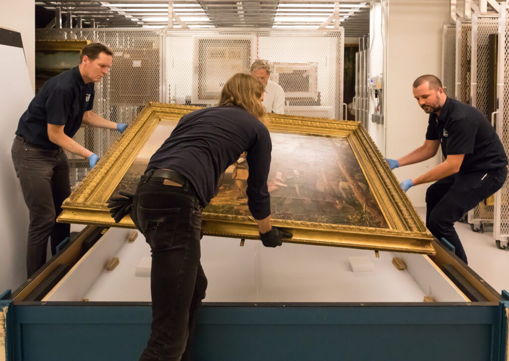 Three people place a painting into a crate.