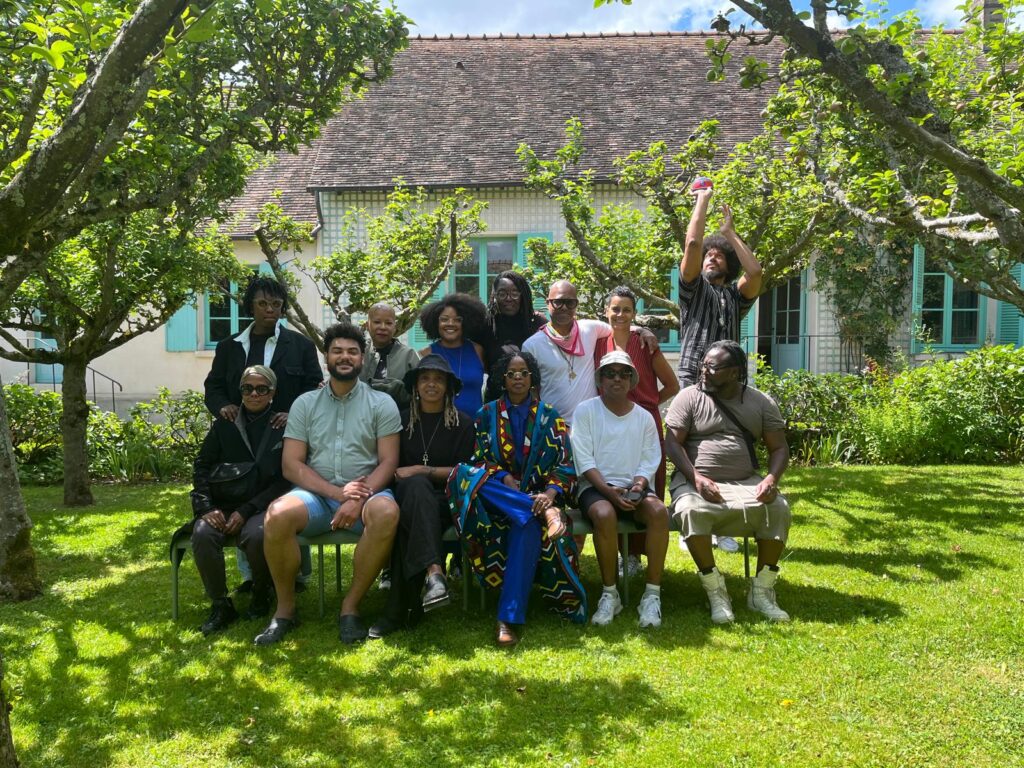 Group of people seated and standing in garden in front of a house.