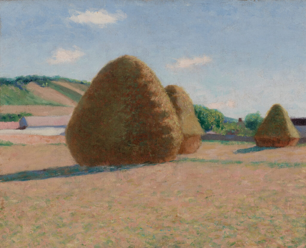 Three haystacks in a field on a sunny day.