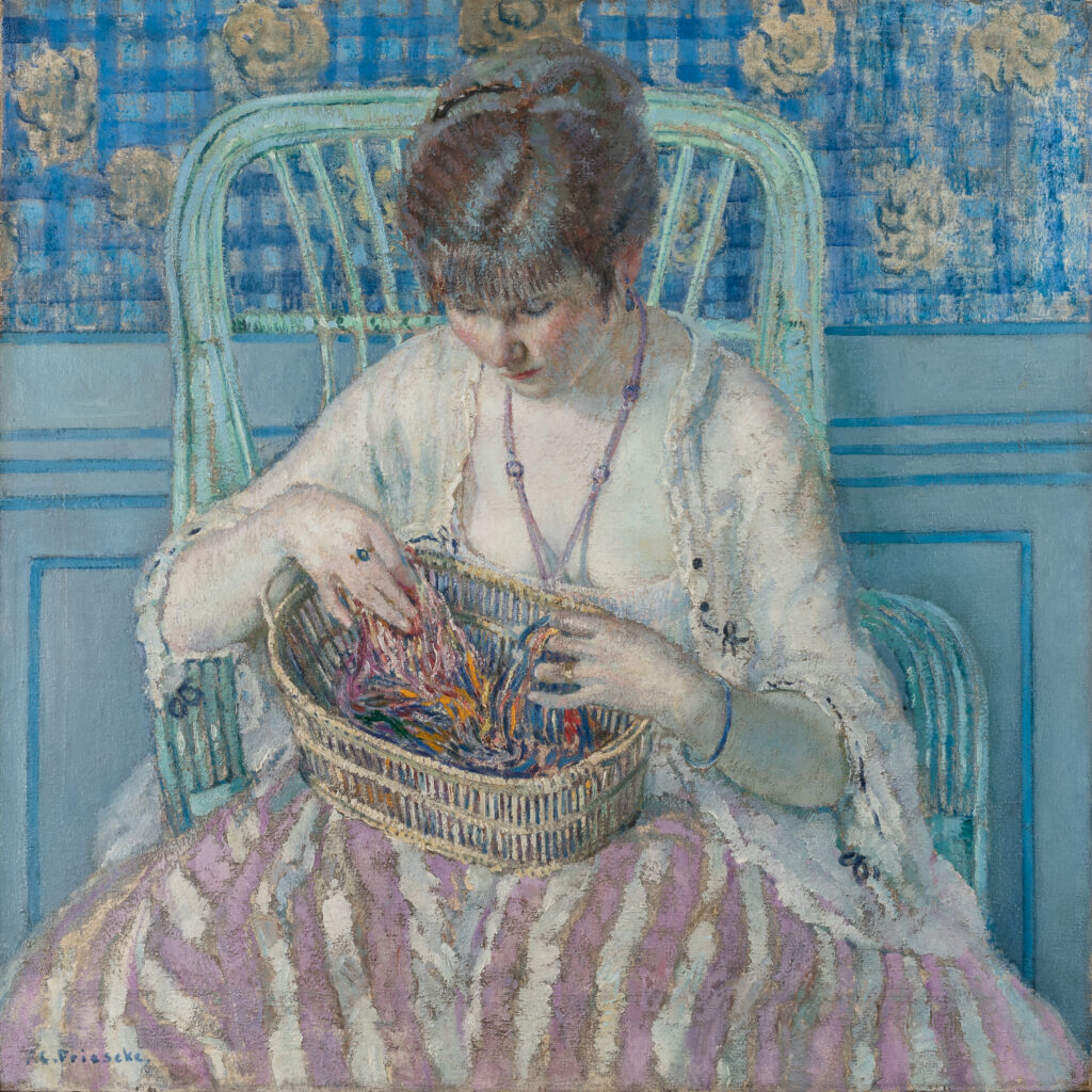 A woman sits in a large green chair unravelling silk thread in a basket in her lap.