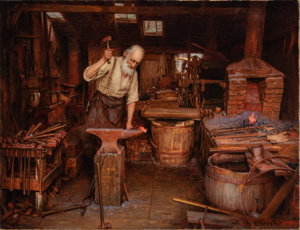A man in a blacksmith studio prepares to hammer a tool onto an anvil.