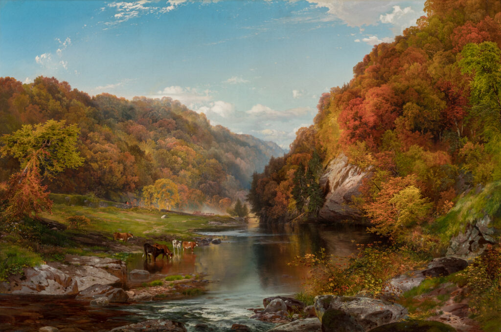A view of a river winding between hills covered in trees. It is autumn, and the trees are brown, orange, red, and green.