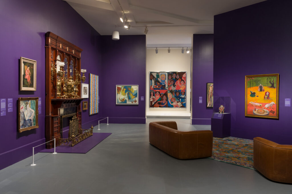 A gallery with purple walls and pieces of artwork hanging up.