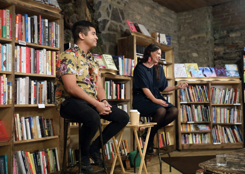 Two people seated on stools in front of bookshelves filled with books.