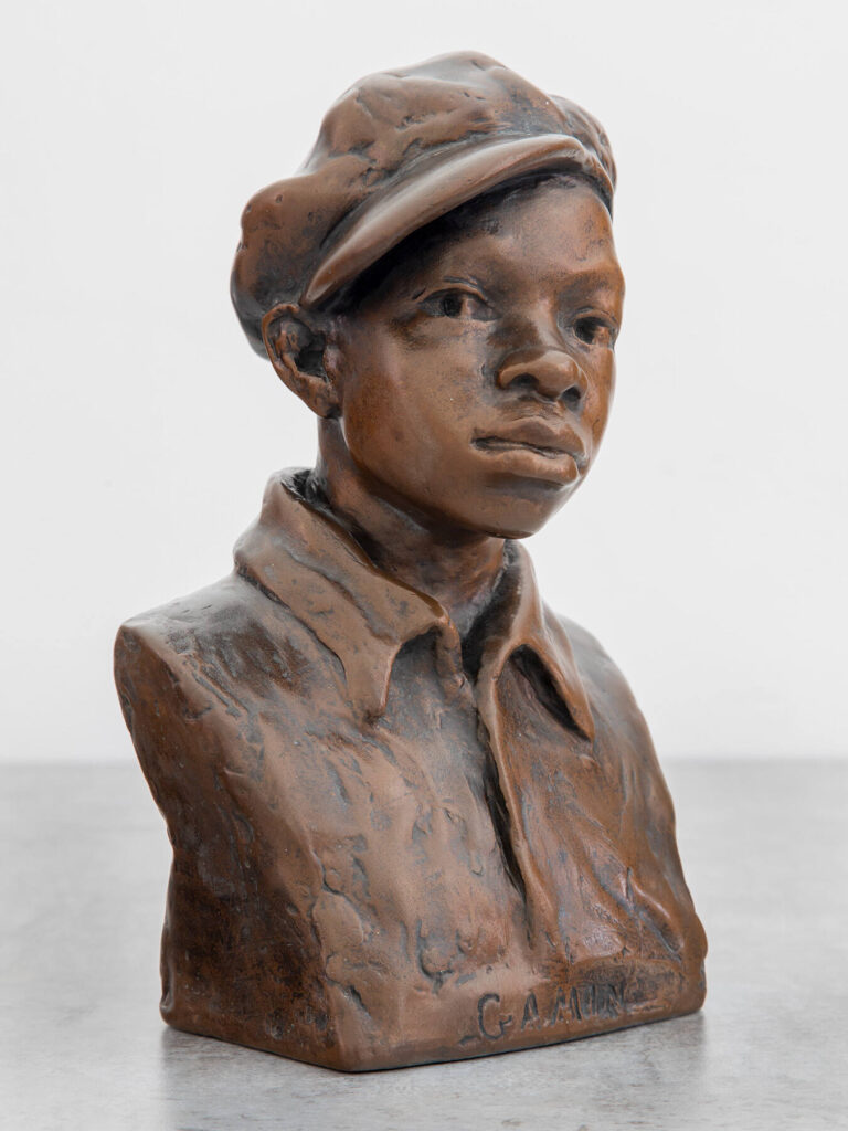 Painted plaster bust of a boy wearing a hat and a collared shirt.