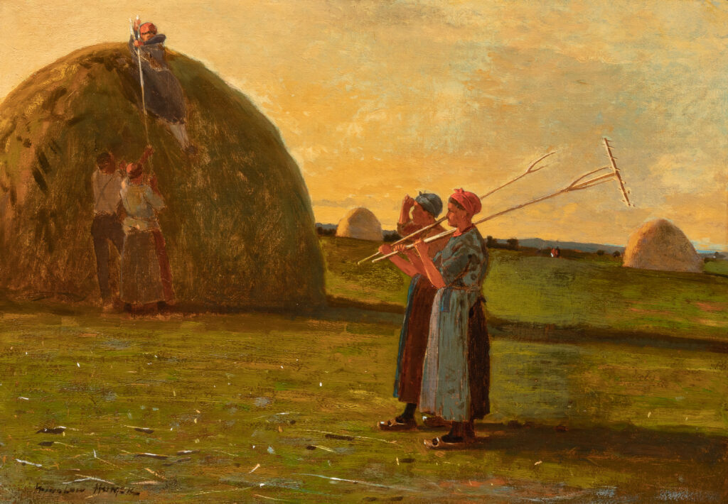 Two women carrying pitchforks walk through a field of haystacks.