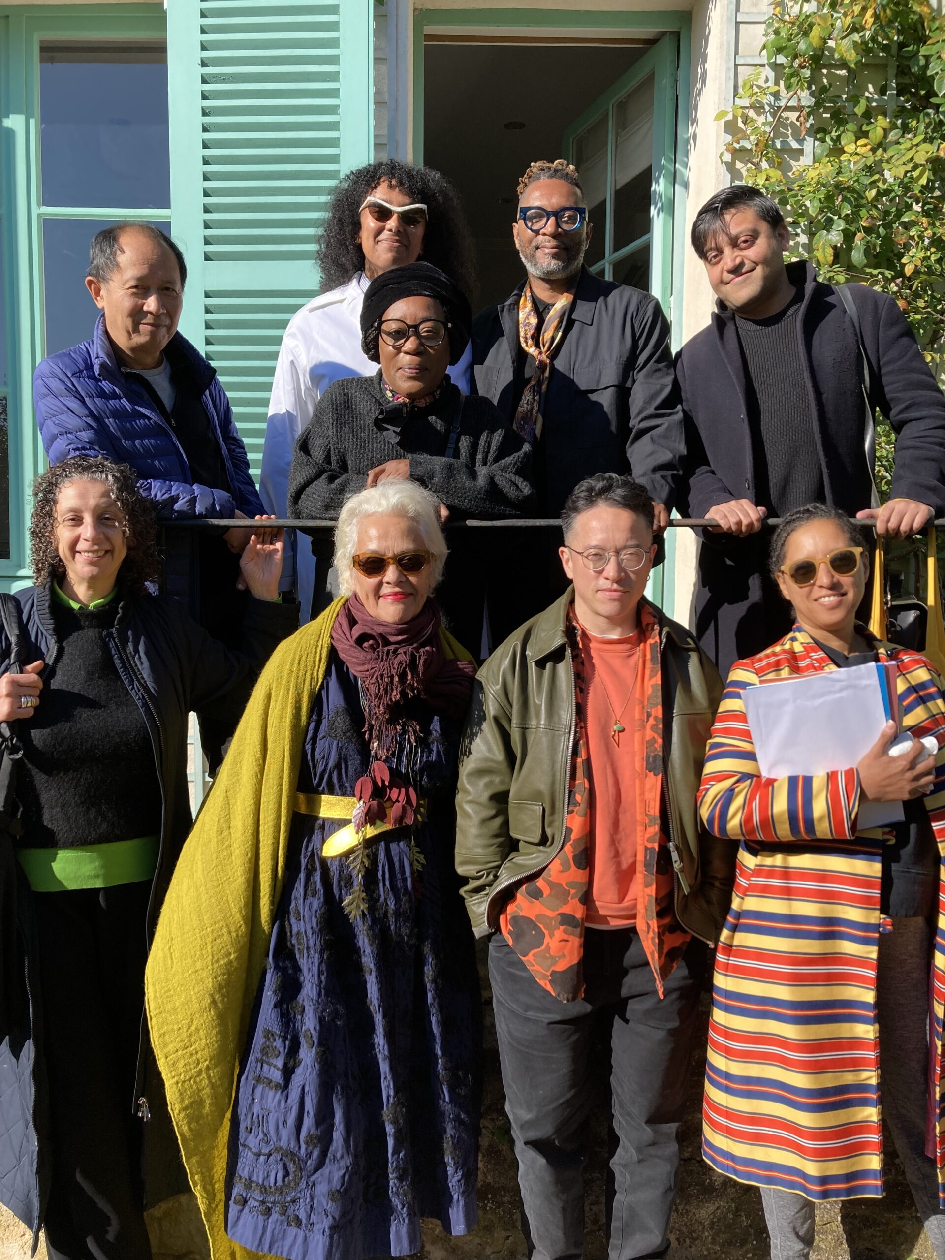 A group of people outside standing on and in front of a porch.
