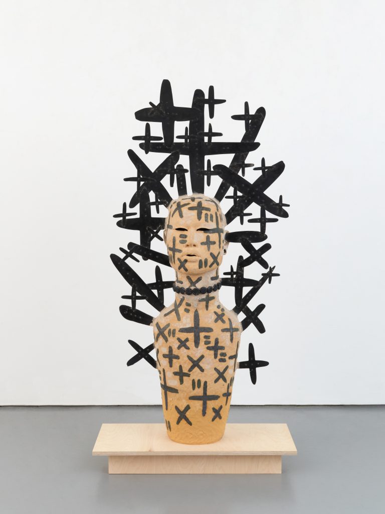 An image of a sculpture in front of a white wall with black drawings on it.
