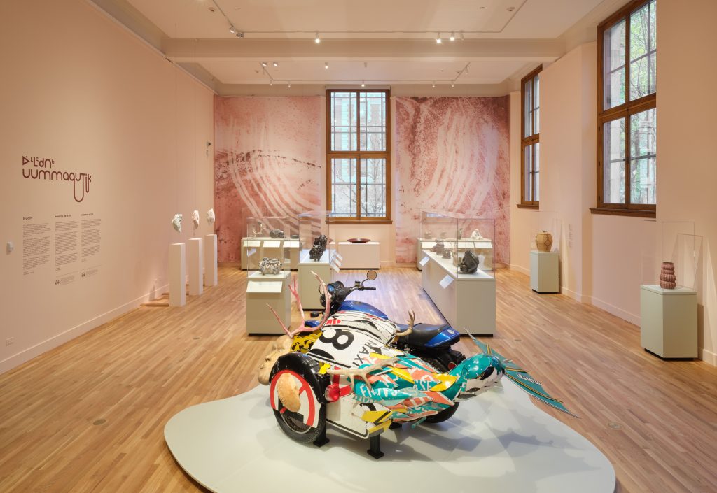 Colorful sculpture set close to the ground with vitrines filled with objects in the background.