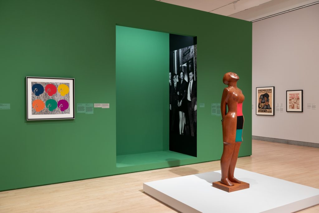 Sculpture on a white plinth in a gallery space with a green wall.