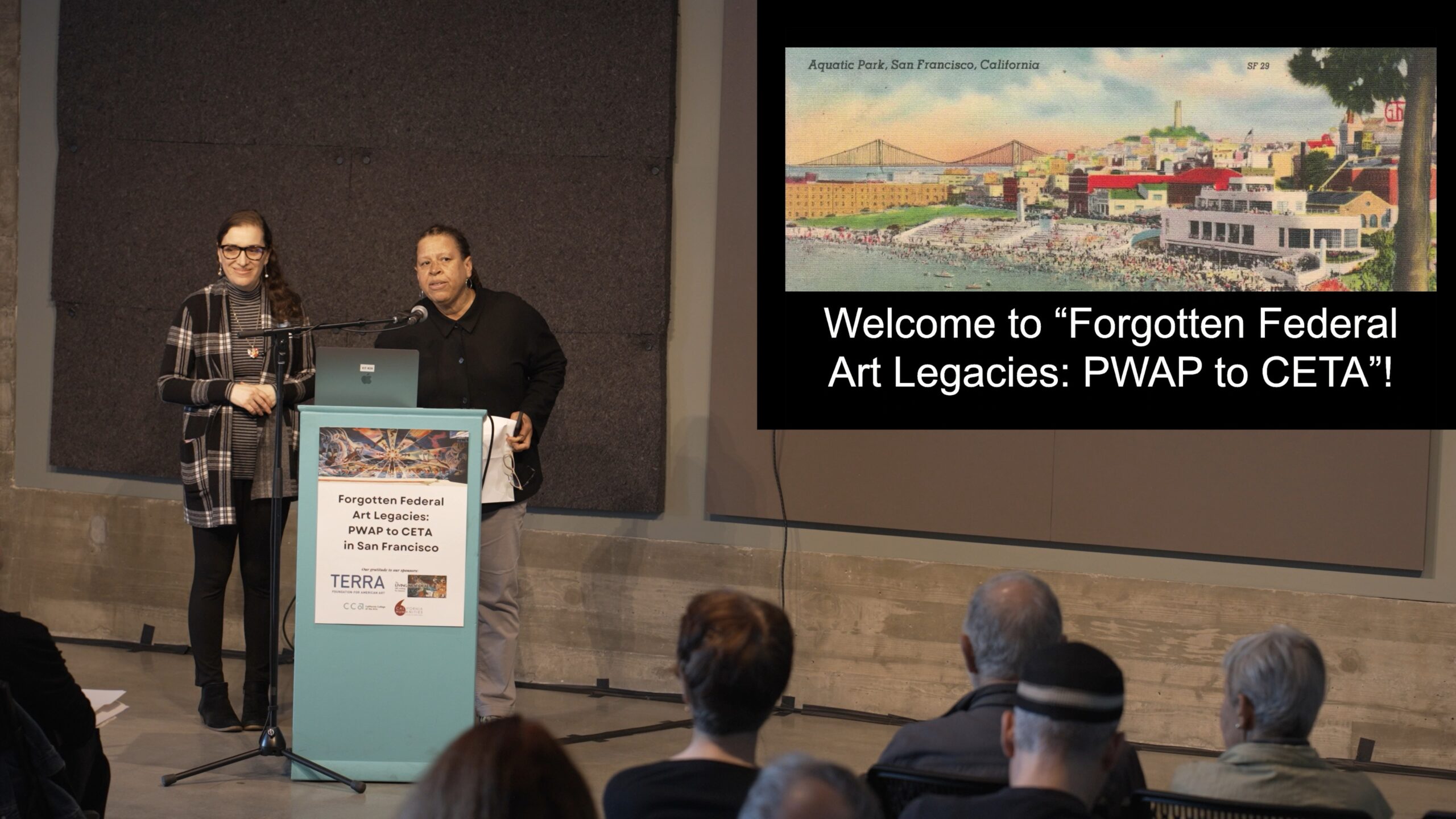 Mary Okin and Jacqueline Francis speaking at a podium with a slide presentation showing on a screen to their left.