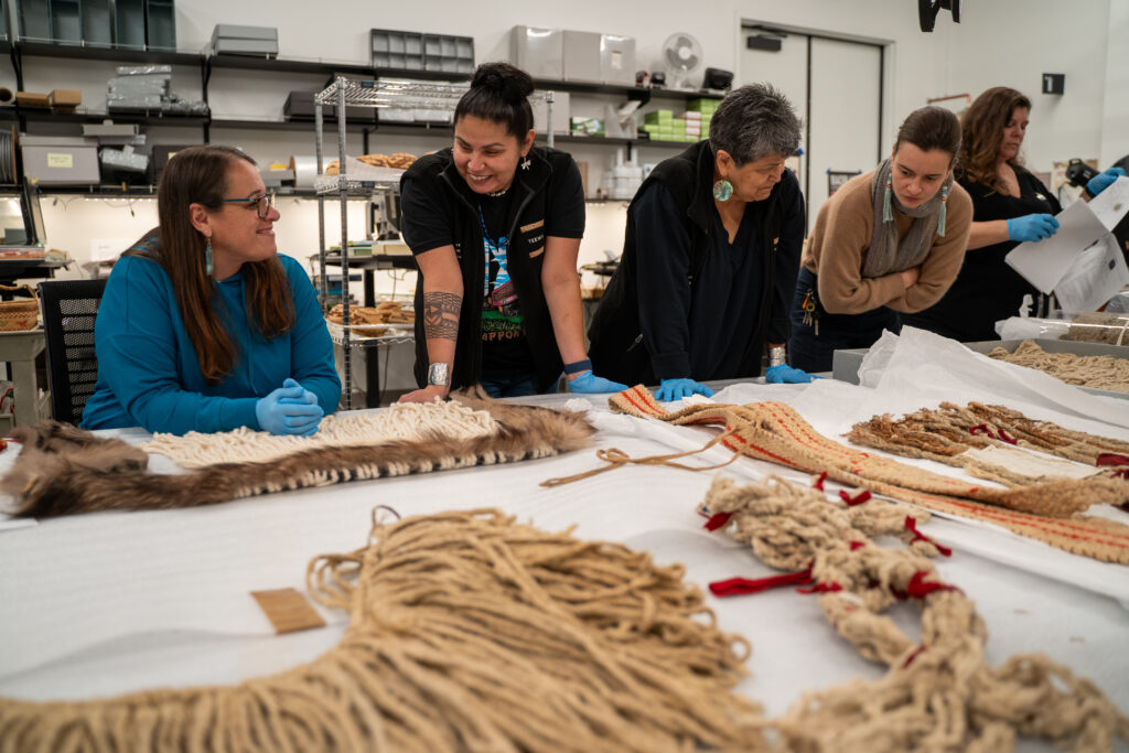 Four people leaning over a table with items from the Burke Museum’s Coast Salish weaving collections.