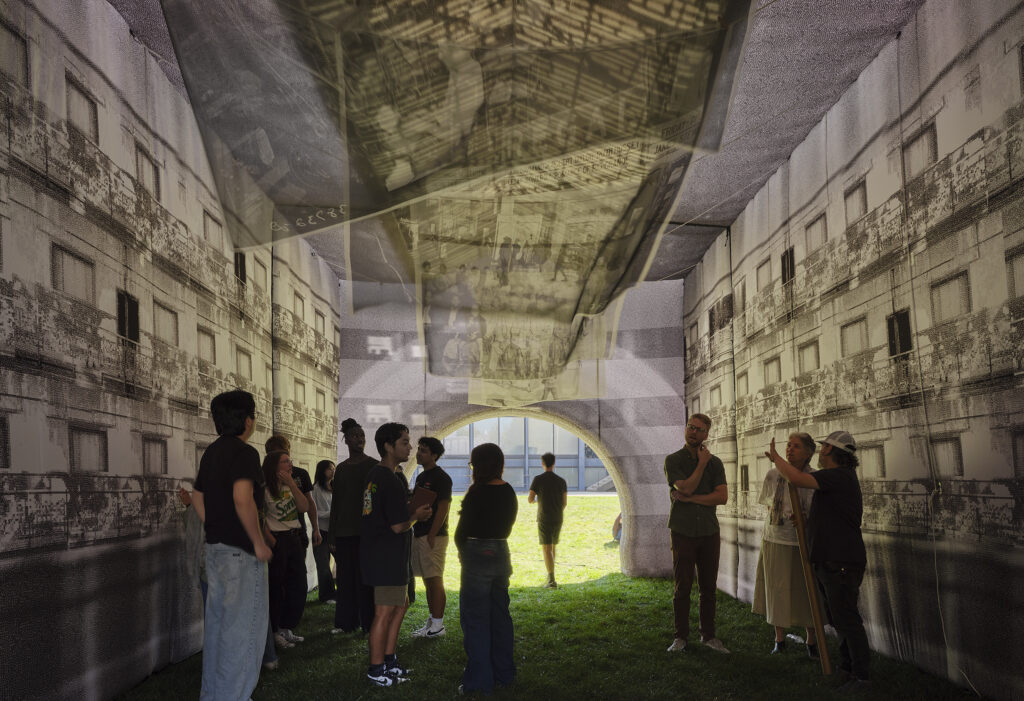 A group of people standing inside a large tent on green grass. Architectural images are projected on the walls and ceiling of the tent.