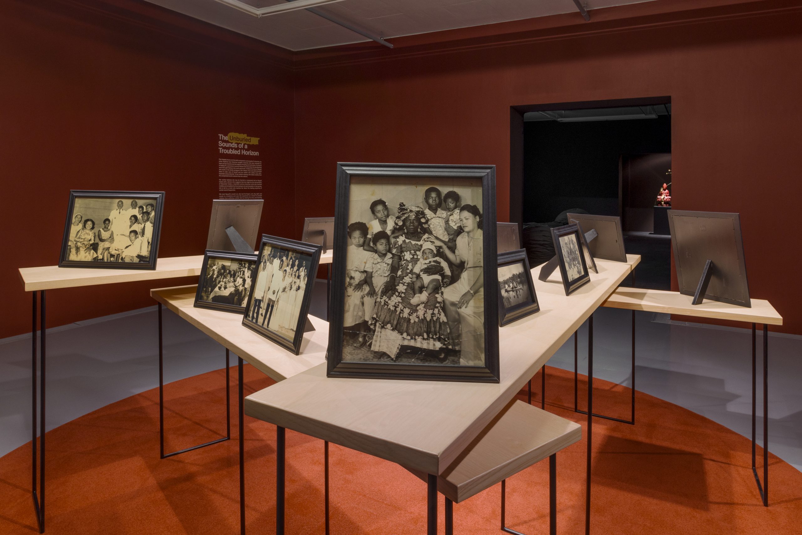 Framed black-and-white photographs placed on many long white tables set at different angles in a room with dark walls.