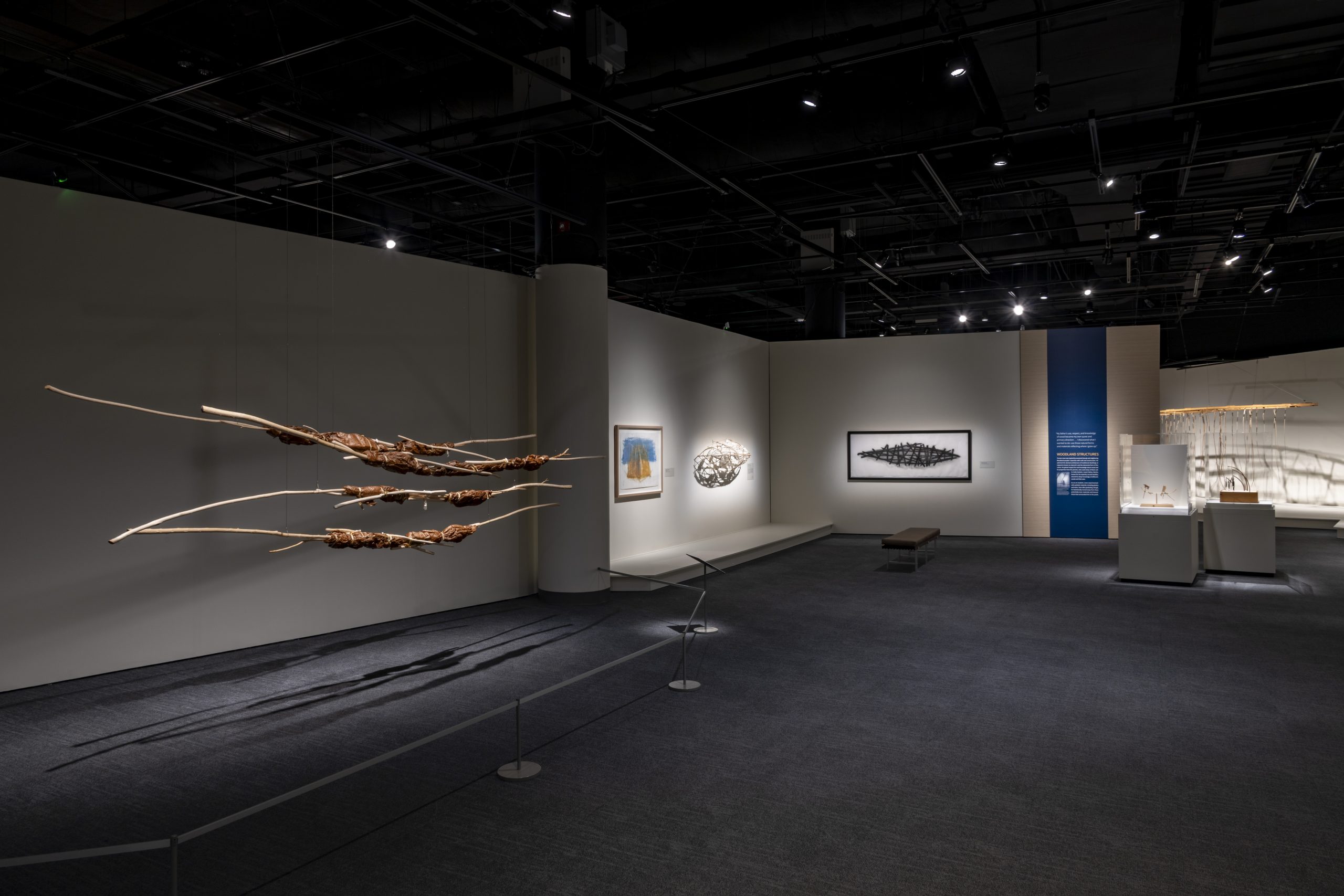 Objects installed in a dark gallery space. Some objects are suspended from the ceiling.